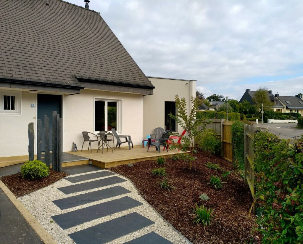 Aménagement final d’un jardin d’entrée avec allée en palis ardoise, terrasse bois et massifs végétalisés paillés près de Rennes